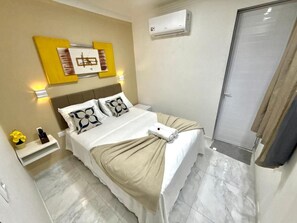 Een keurig opgemaakt slaapkamer met een bed, nachtkastjes, een wandairconditioner en een deur.