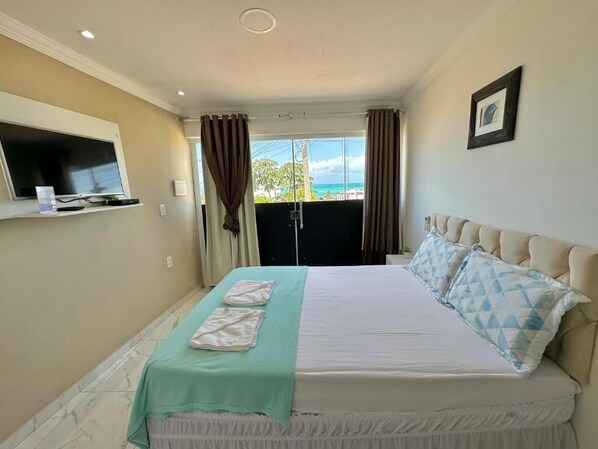 Een hotelkamer met een bed, een televisie, een raam met gordijnen en uitzicht op de oceaan.