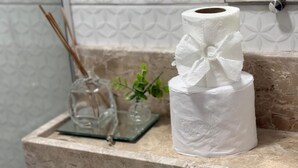 Et badeværelse med bordplade i marmor, toiletpapir, en glasvase med plante og en pynteting.