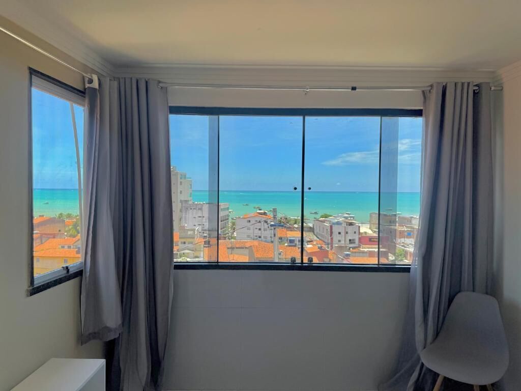 A room with a large window, a chair, and a view of the sea and buildings.