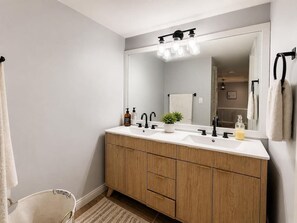 A bathroom with a double sink, wooden vanity, and a large mirror. - University Condo (Gainesville)