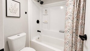 A bathroom with a toilet, a bathtub, a showerhead, and a framed picture on the wall. - University Condo (Gainesville)