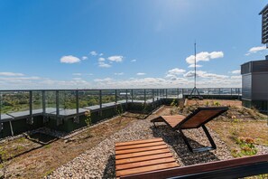A rooftop terrace with a clear view of the cityscape, equipped with wooden loungers and a metal railing. - Horizon 653 by Grand Apartments  (Gdańsk)