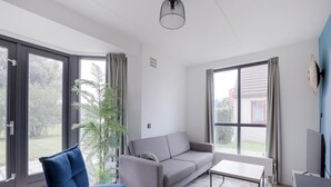 Ein modernes Wohnzimmer mit einem grauen Sofa, einem blauen Sessel, einem Couchtisch und großen Fenstern.