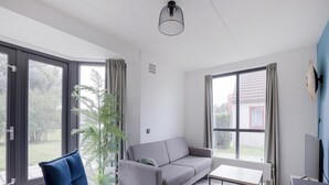 Een moderne woonkamer met een bank, een blauwe stoel, een salontafel en grote ramen.