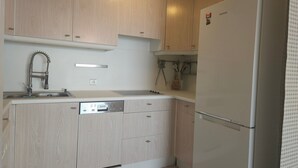 A kitchen with wooden cabinets, a stainless steel sink, and a white refrigerator. - Central Juan-les-Pins Colombier 1-Bedroom with Sea View, Parking (Antibes)