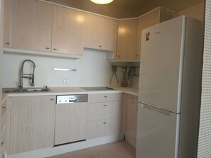 Una cocina con armarios de madera, un lavamanos de acero inoxidable y un refrigerador blanco.