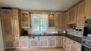 A kitchen with wooden cabinets, a window, a toaster, and an oven. - Beautiful Villa in private estate with 5 bedrooms, swimming pool, panoramic view (Villeneuve-Loubet)