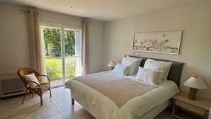 A bedroom with a large bed, a chair, a nightstand, and a window with a view of greenery. - Beautiful Villa in private estate with 5 bedrooms, swimming pool, panoramic view (Villeneuve-Loubet)