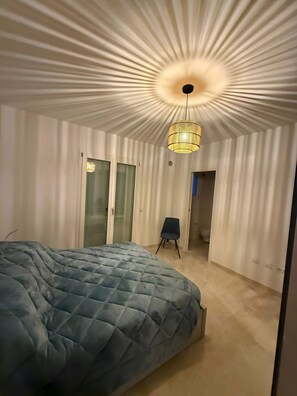 Un dormitorio con cama, una silla, una lámpara colgante y una puerta.