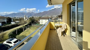 Un balcon avec vue sur les montagnes, une table avec des chaises et une voiture garée à l’extérieur.