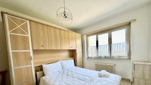 Une chambre à coucher avec un lit, une armoire en bois, une fenêtre donnant sur un paysage agréable et un luminaire suspendu.
