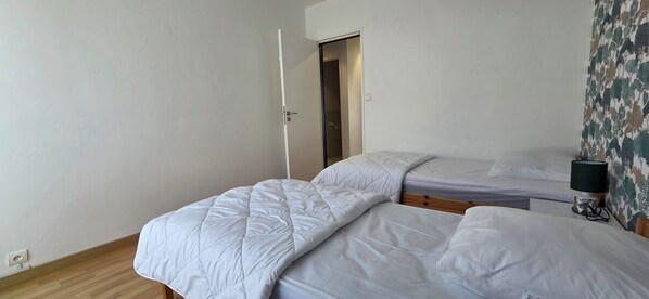 Een slaapkamer met twee eenpersoonsbedden, een houten vloer, een deur en een behang met patroon.