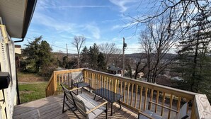 A wooden deck with a metal table and chairs, overlooking a residential area with trees and houses.