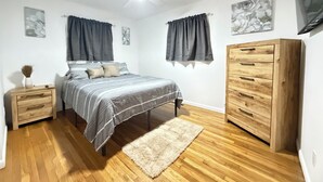 A bedroom with a bed, nightstands, a wooden dresser, a ceiling fan, and artwork on the walls.