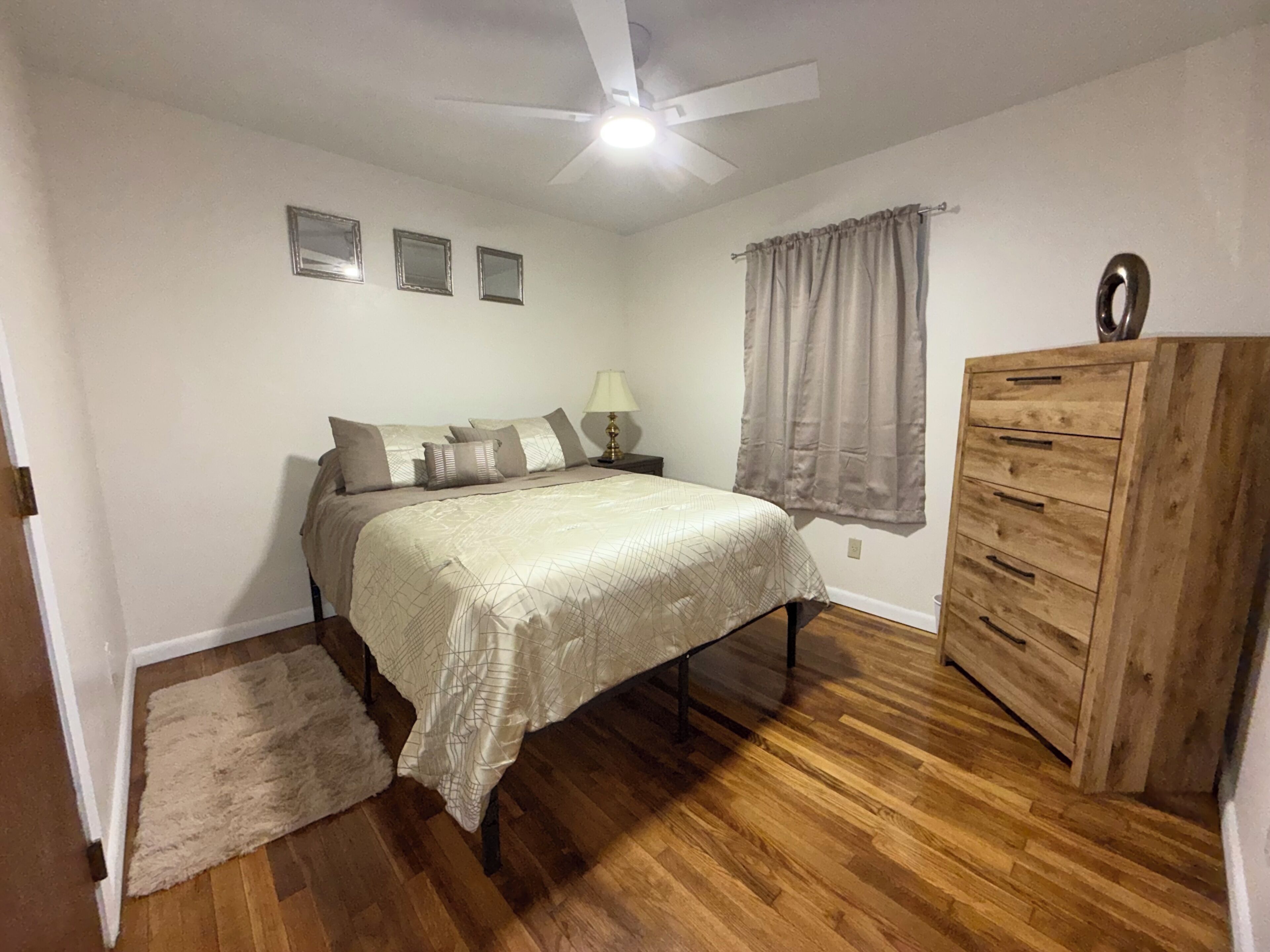 A bedroom with a bed, nightstand, dresser, ceiling fan, and wall-mounted lights.