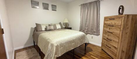 A bedroom with a bed, nightstand, dresser, ceiling fan, and wall-mounted lights.