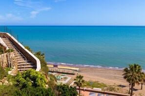 Vista costera con una playa, una escalera que baja a la playa y una zona cubierta con un cartel.