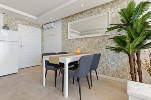 Ein Essbereich mit einem weißen Tisch, vier grauen Stühlen, einer weißen Bank, einer Zimmerpflanze und einem an der Wand befestigten Spiegel.