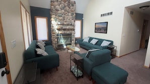 A living room with a stone fireplace, two green sofas, a coffee table, and a framed picture on the wall.
