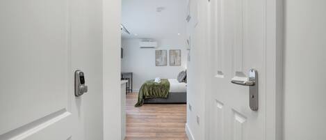 A hallway leading to a bedroom with a bed, a desk, and a wall-mounted air conditioner.