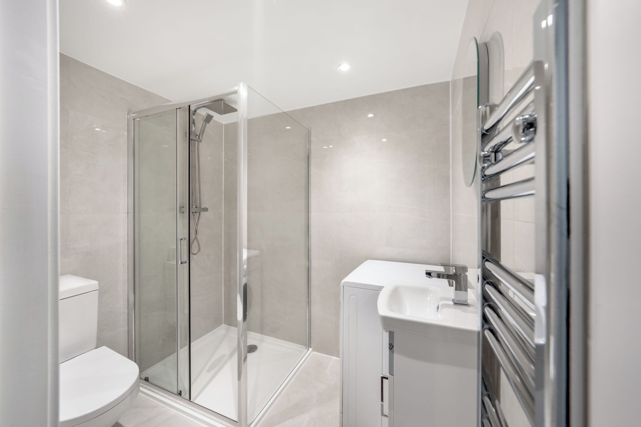 Un baño moderno con ducha envuelta en vidrio, inodoro blanco y lavamanos con grifo cromado.
