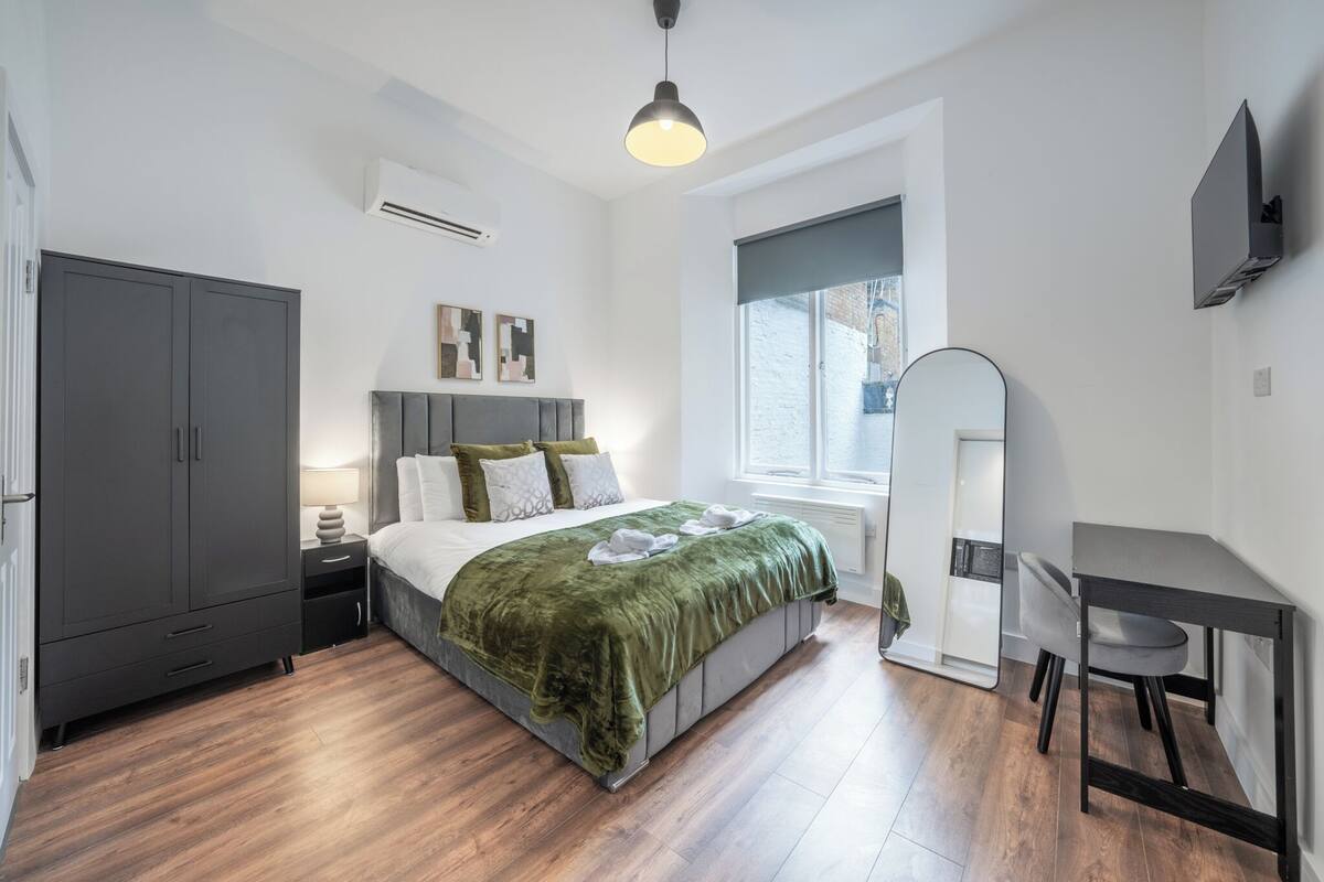 A modern bedroom with a bed, wardrobe, bedside table, and a desk with a chair.
