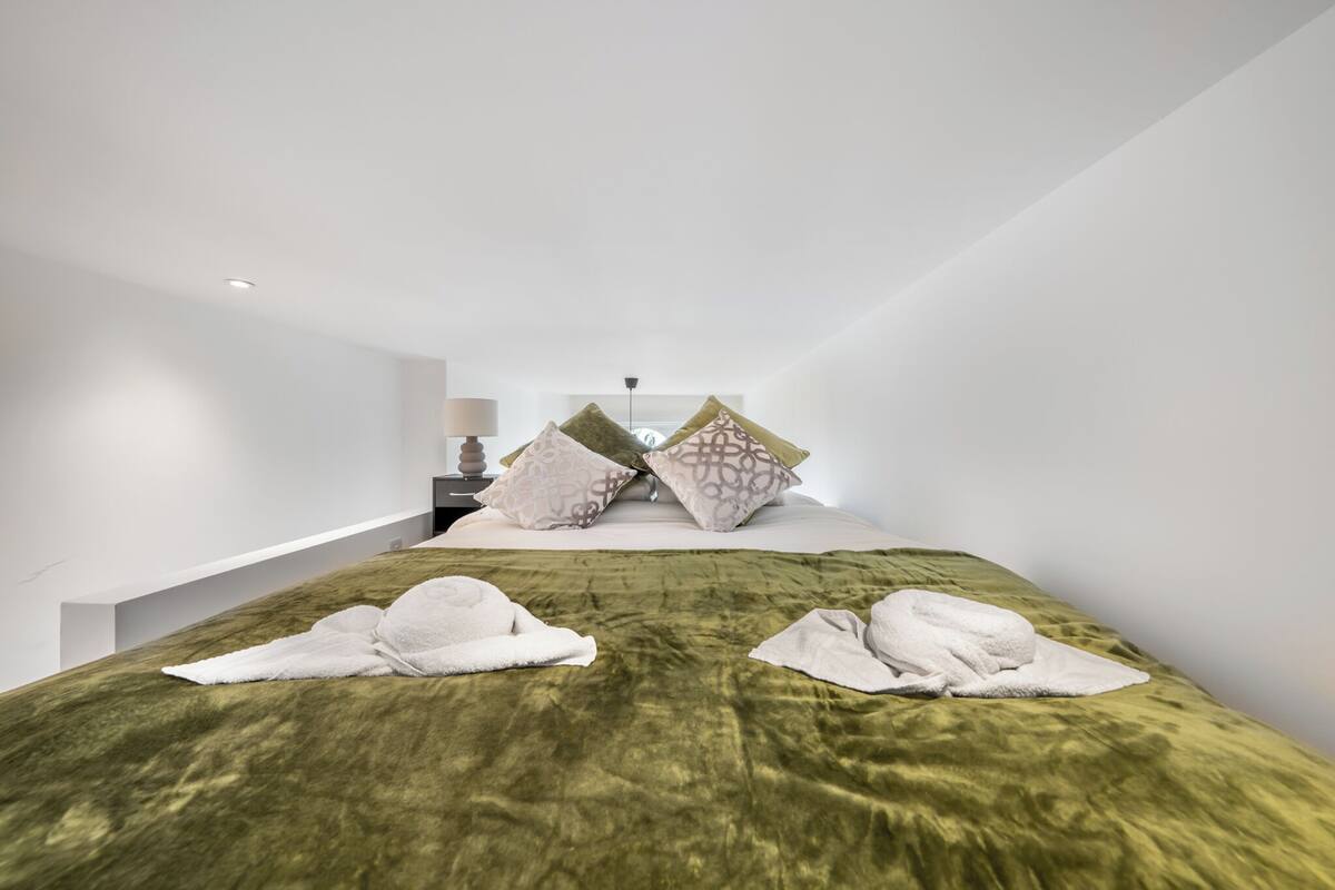 A modern bedroom with a green velvet bedspread, white towels, and patterned pillows.