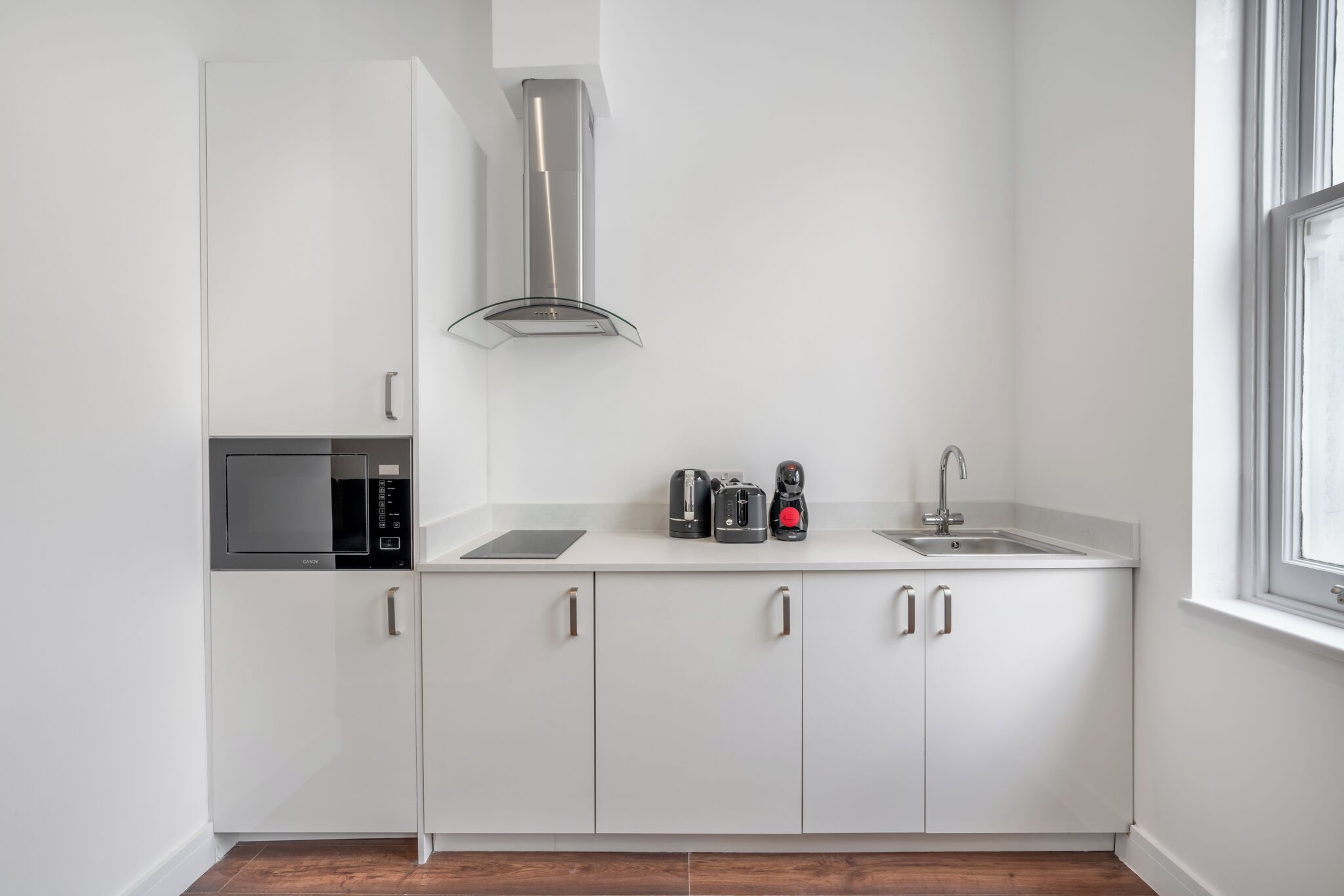 Una cocina moderna con armarios blancos, una campana de acero inoxidable, microondas, tostadora y fregadero.