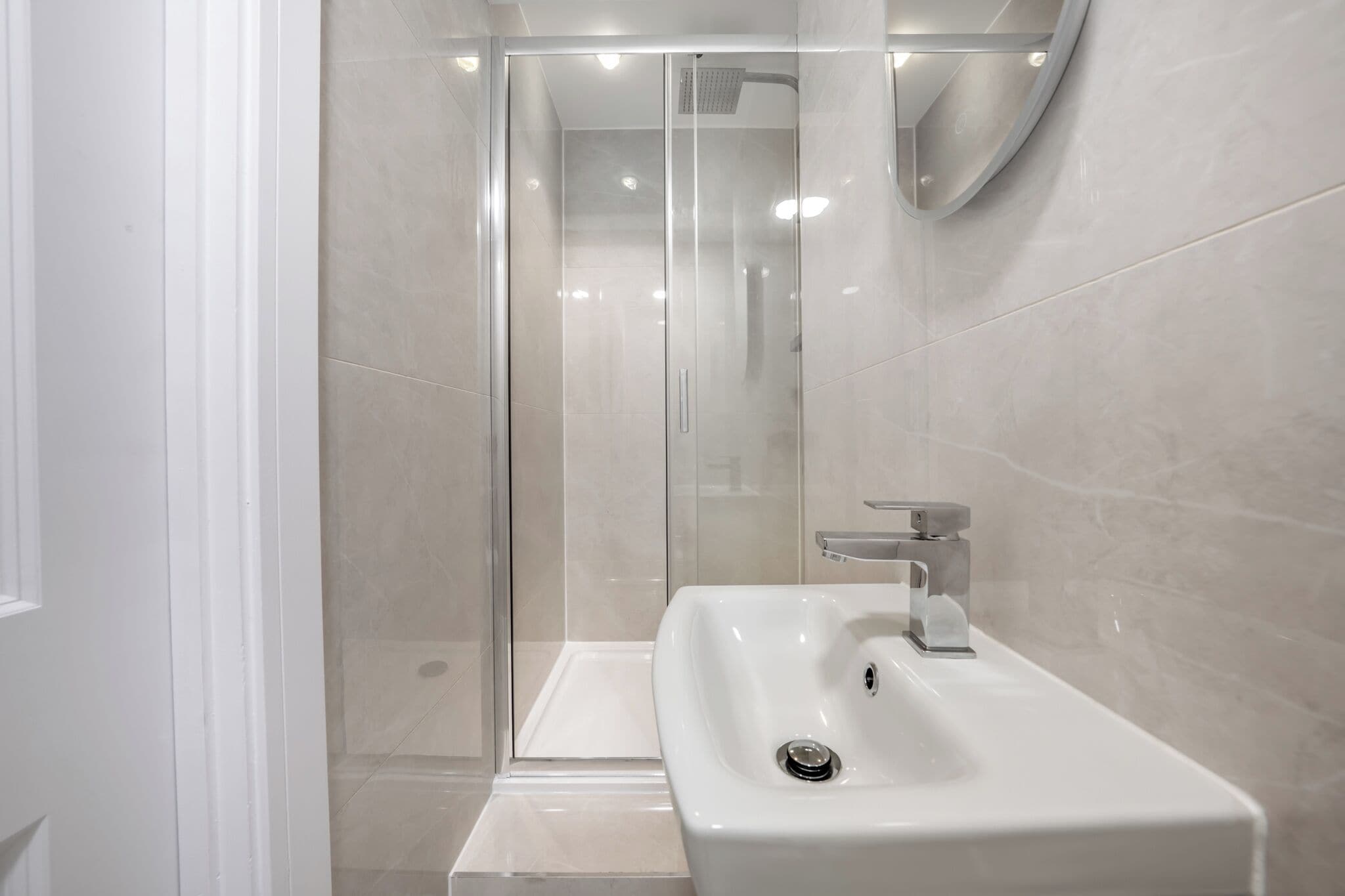 A modern bathroom with a glass-enclosed shower, a white sink, and a mirror.
