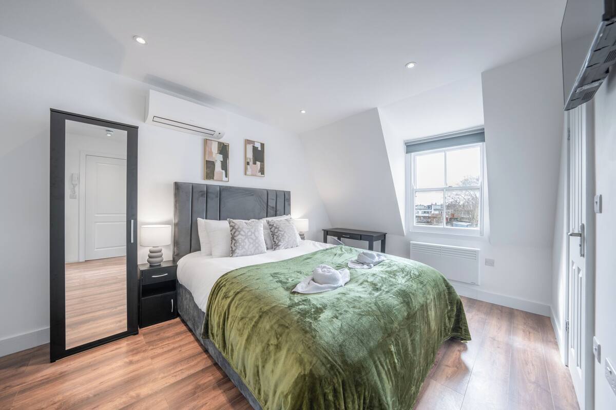 A modern bedroom with a bed, bedside tables, a mirror, and a window.