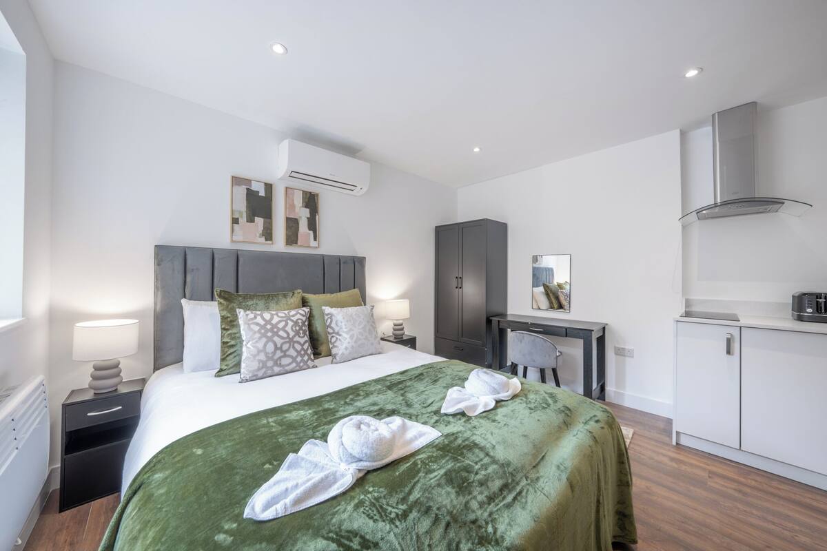 A modern hotel room with a bed, a desk, a wardrobe, and an air conditioning unit.