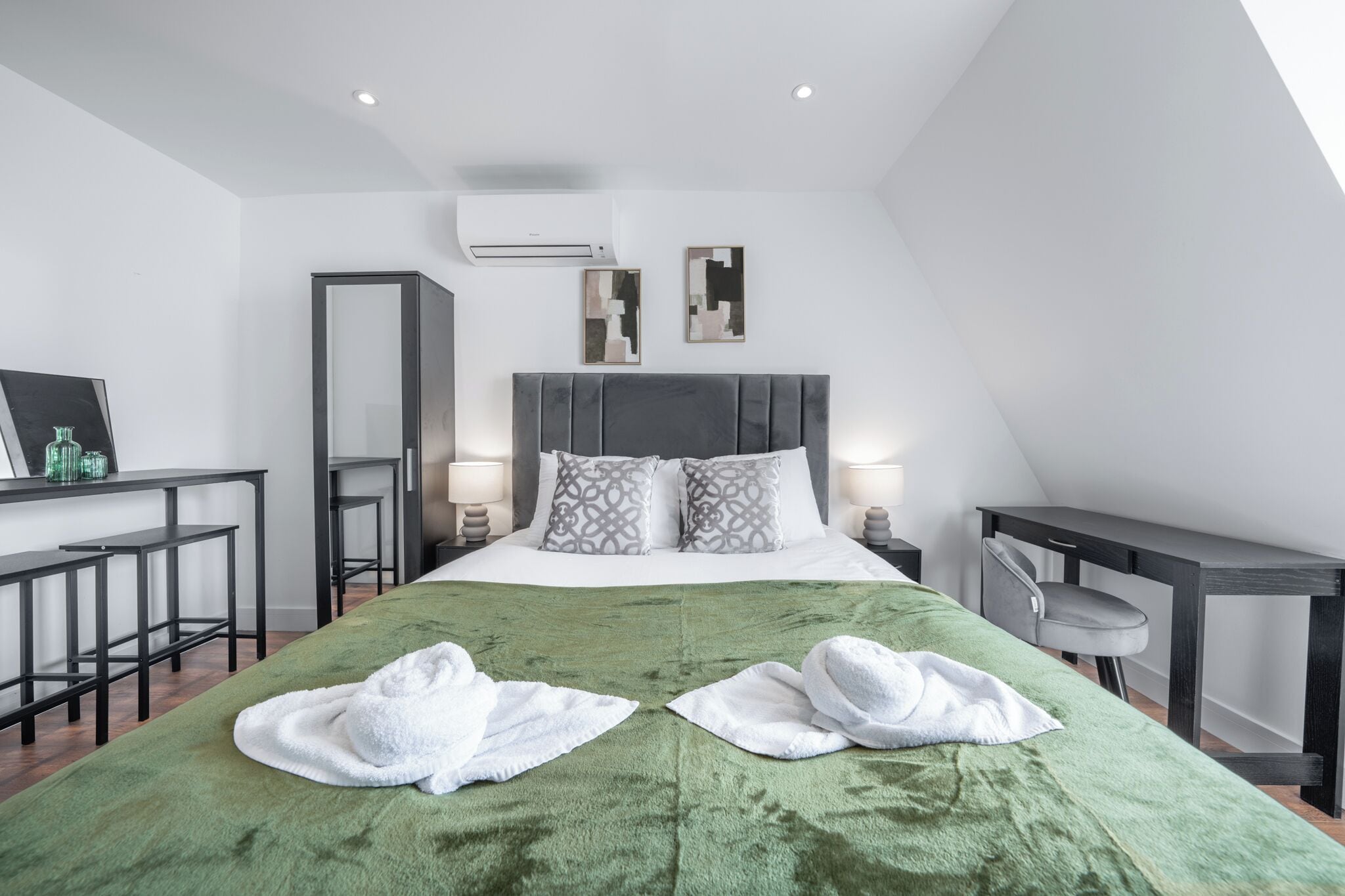 Ett modernt hotellrum med en stor säng, ett skrivbord, en stol och en spegel.