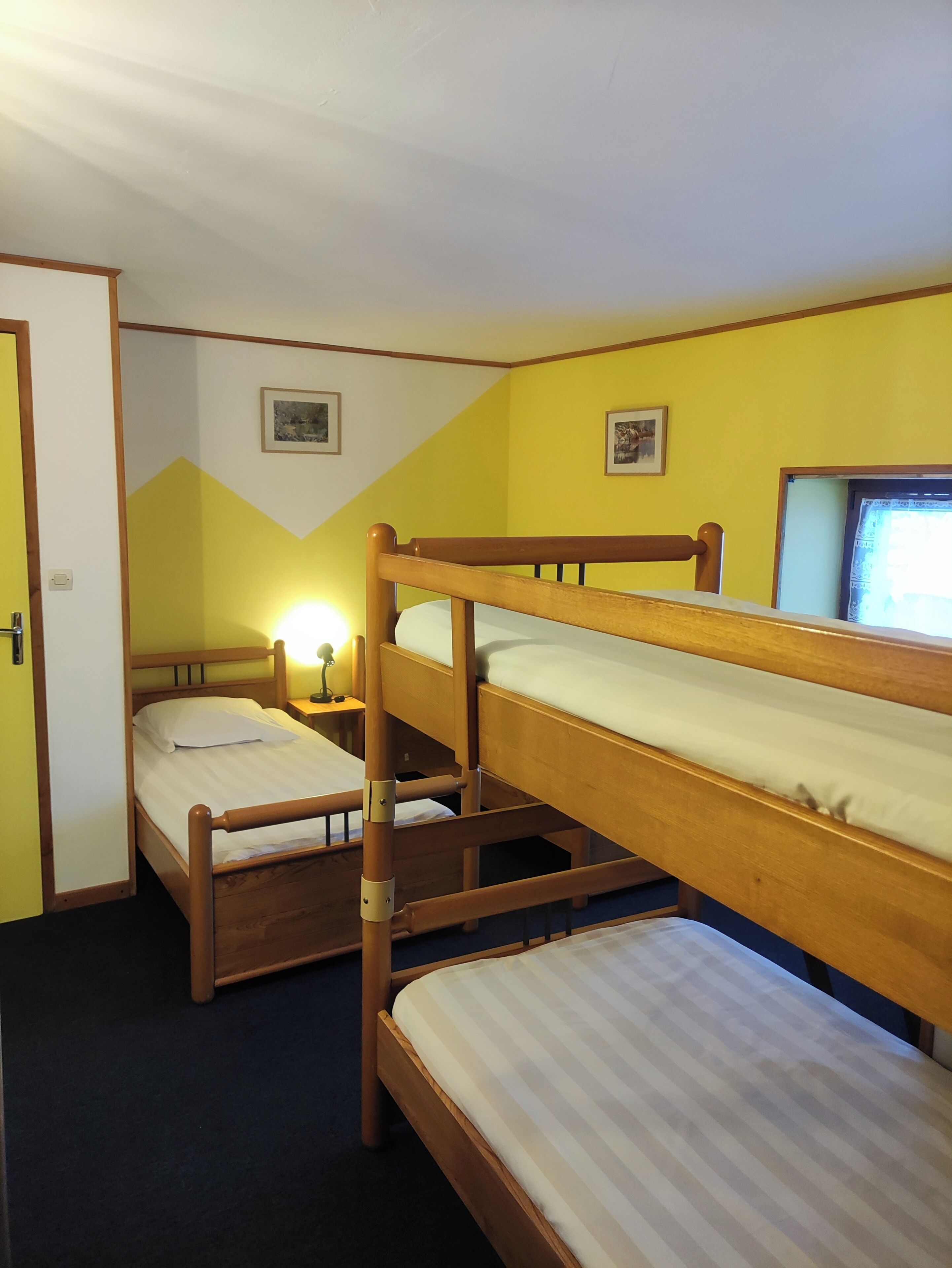 A room with bunk beds, a door, a wall-mounted picture, and a bedside table with a lamp.