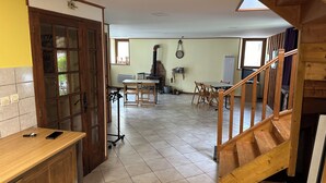 Une cuisine spacieuse avec des meubles de rangement en bois, un coin repas avec une table et des chaises, et un escalier en bois menant à l’étage supérieur.