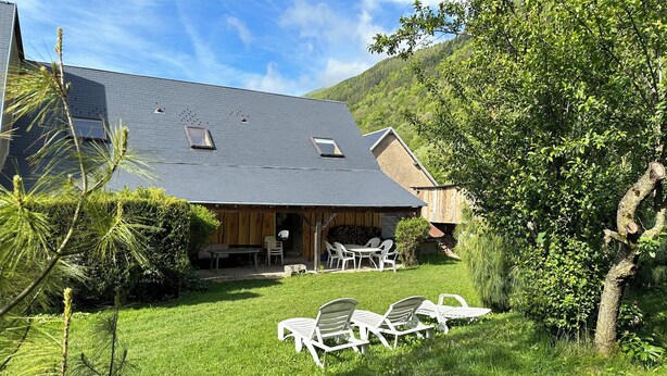 Une maison avec un toit en pente, une terrasse dotée de mobilier d’extérieur et une pelouse bien entretenue.