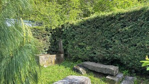 Une fontaine en pierre, un banc en pierre et un sentier en pierre, le tout dans un jardin luxuriant et verdoyant.