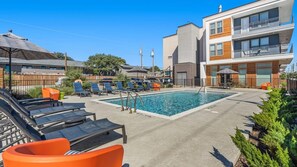 A swimming pool with lounge chairs and umbrellas, surrounded by modern buildings. - Landing Apartments near Dallas Medical District (Dallas)