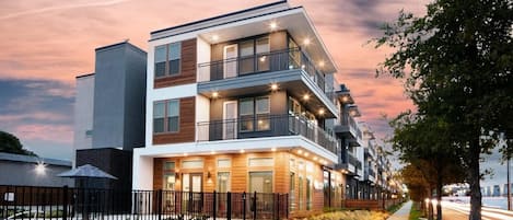 A modern multi-story residential building with balconies, a gated entrance, and a landscaped front yard.