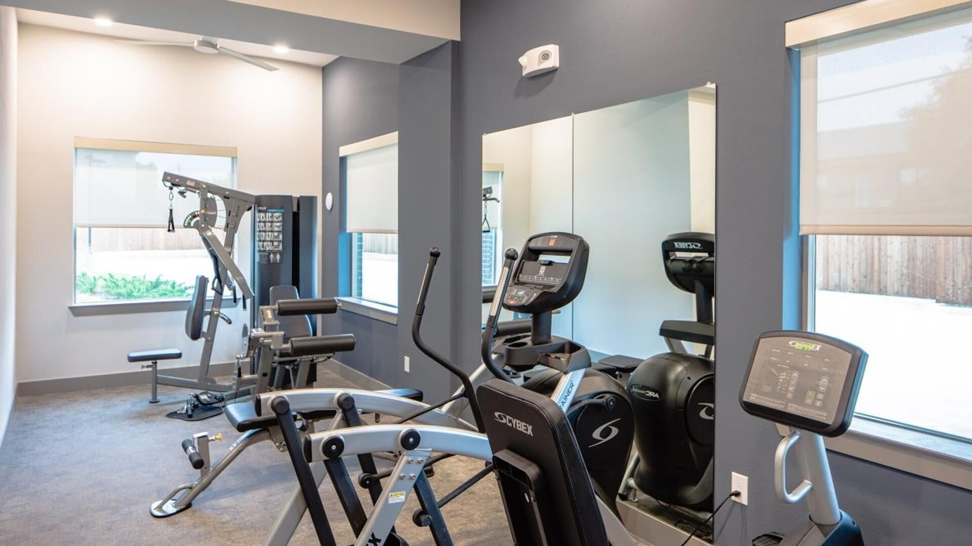 A gym with exercise equipment, large windows, and a mirror.