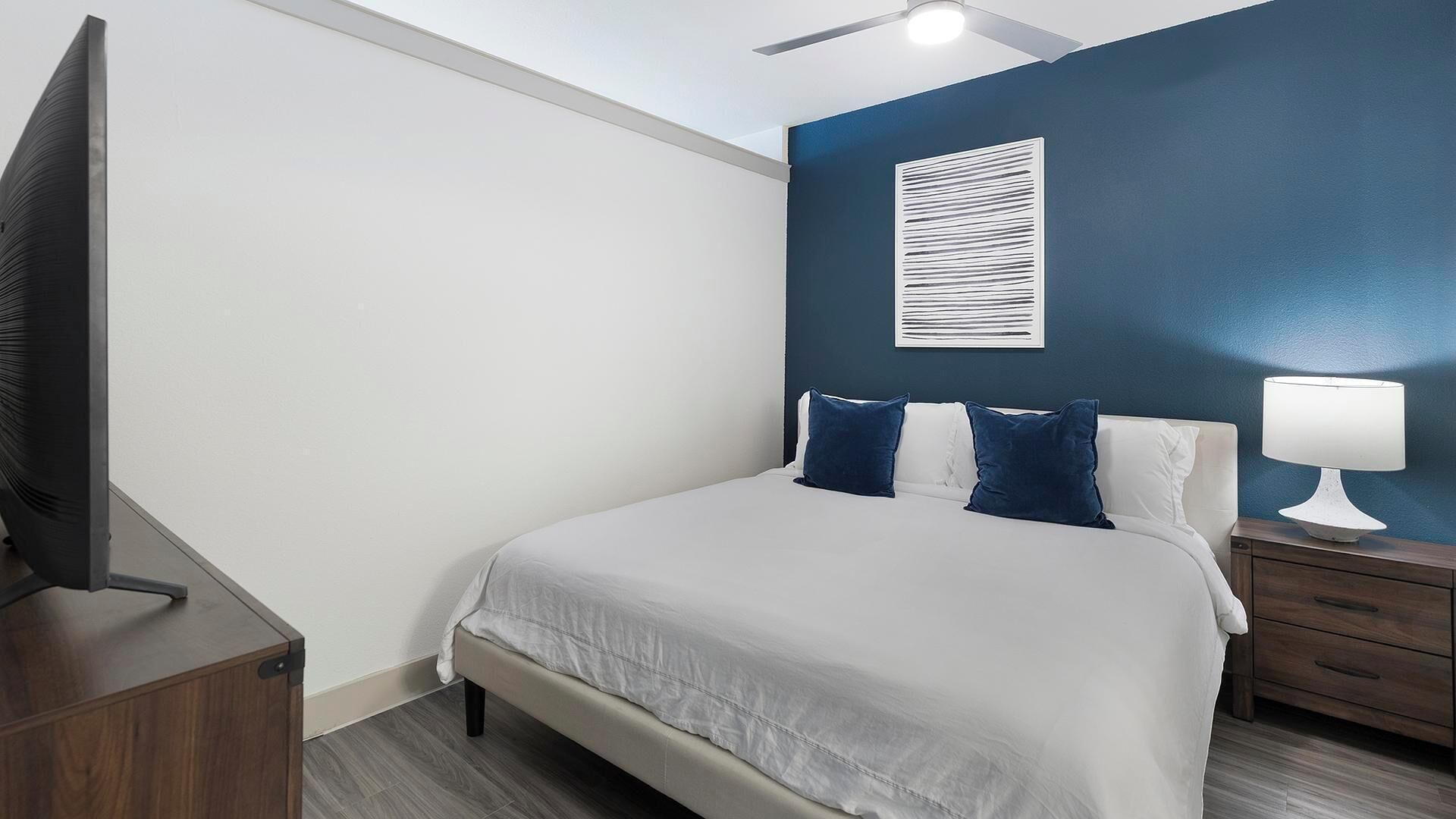 Ein Schlafzimmer mit einem Bett, einem Nachttisch, einer Lampe, einem Fernseher und einem Deckenventilator.