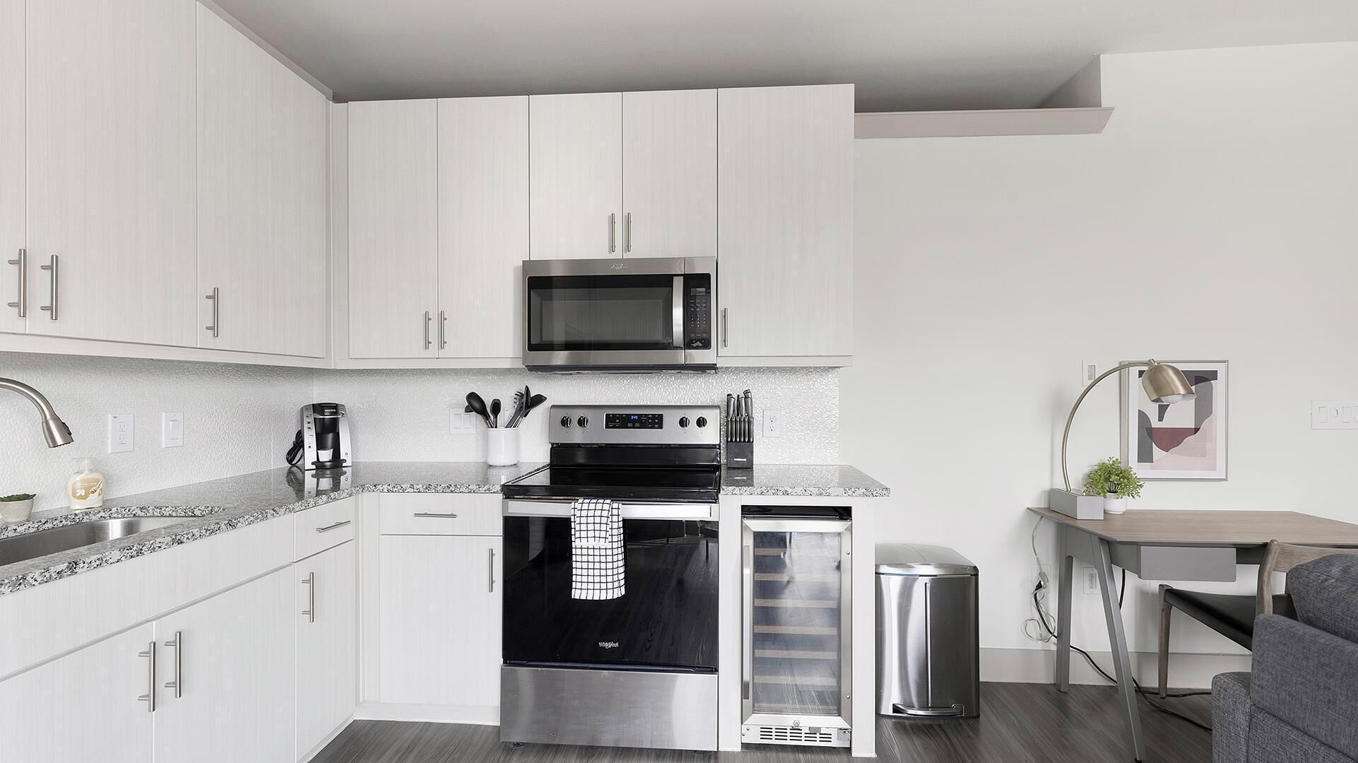 Een moderne keuken met witte kastjes, roestvrijstalen apparatuur, een magnetron, oven en een koffiezetapparaat.