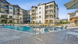 A modern apartment building with a swimming pool, outdoor seating, and a covered patio area.