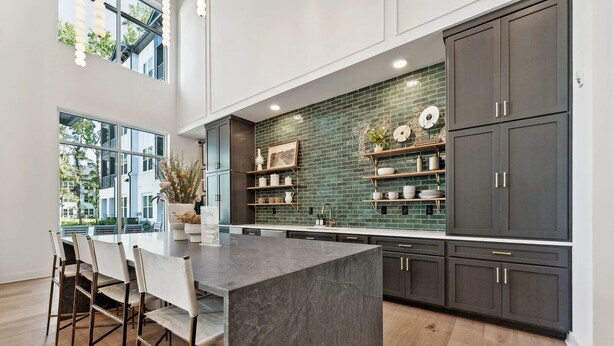 A modern kitchen with a large island, dark cabinets, and a green backsplash.