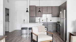 A modern kitchen with dark cabinets, a stainless steel refrigerator, and a white island.