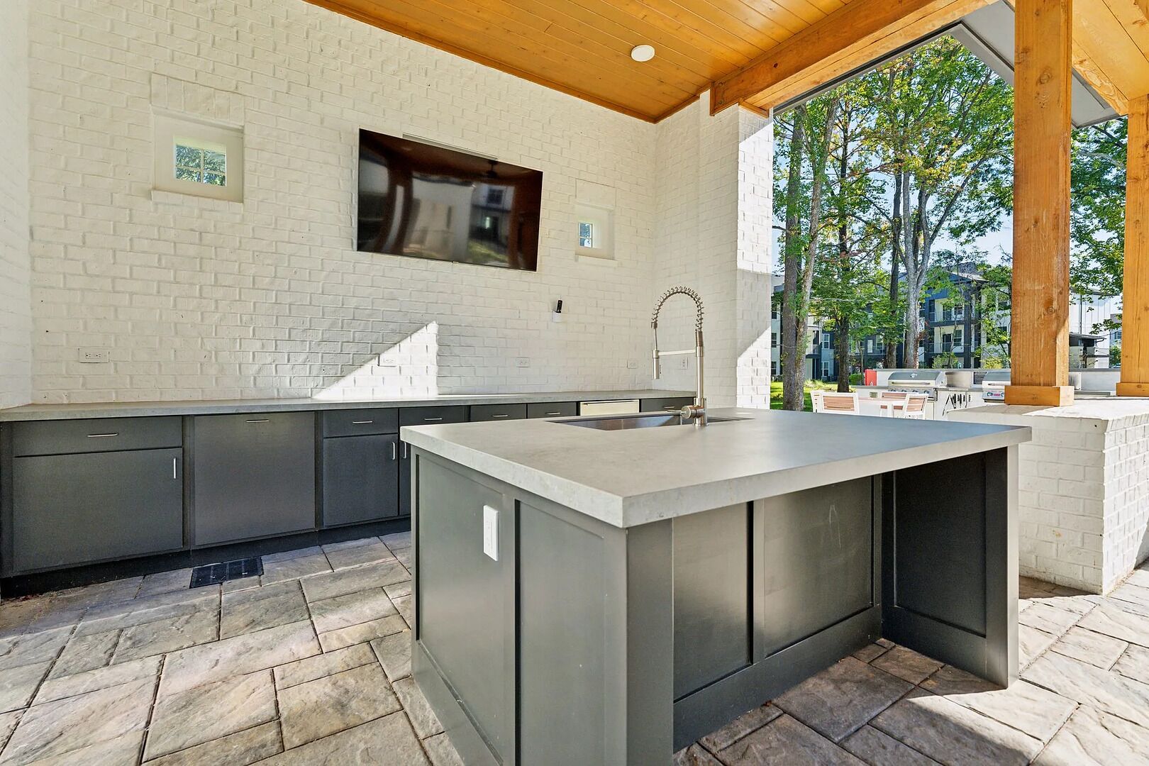 A modern kitchen with a large island, grey cabinetry, and a window overlooking a garden.