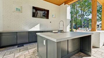A modern kitchen with a large island, grey cabinetry, and a window overlooking a garden.