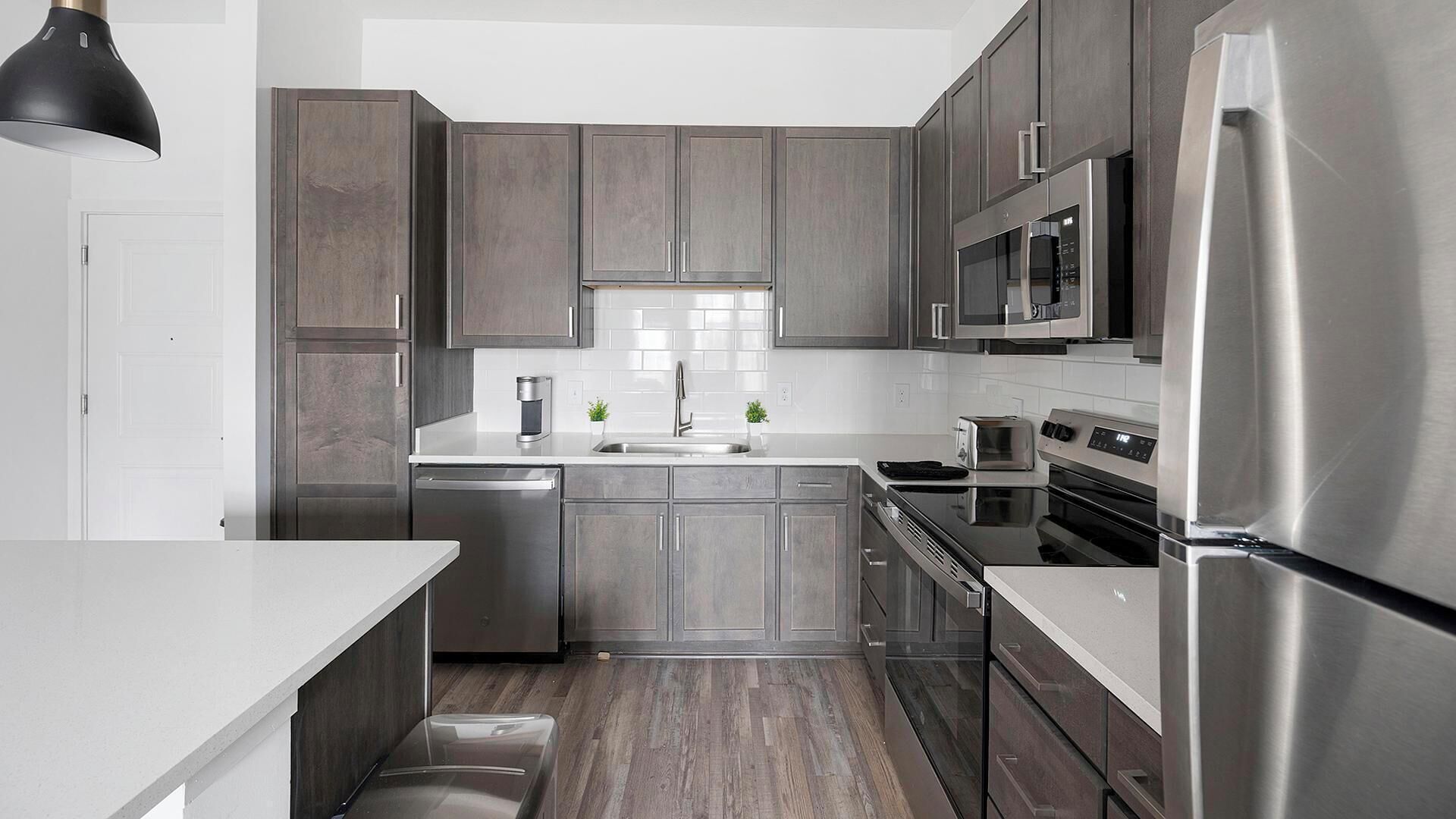 Una cocina moderna con armarios grises, electrodomésticos de acero inoxidable y encimera blanca.