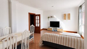 Un dormitorio con cama, televisor, escritorio y sillas, y una puerta.