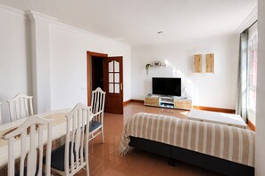 Ein Schlafzimmer mit einem Bett, einem Fernseher, einem Schreibtisch mit Stühlen und einer Tür.